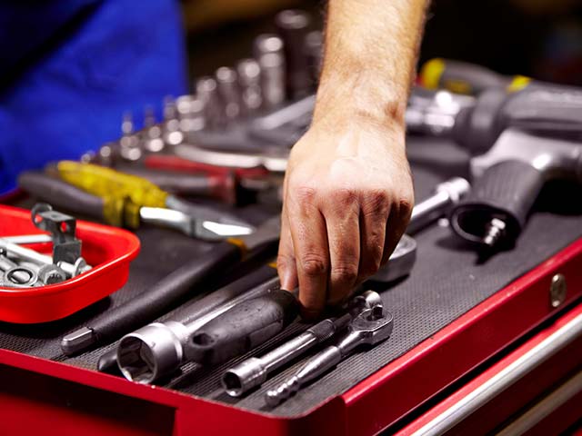 A hand reaching for a tool on a red tool cart with various wrenches and a cordless drill.