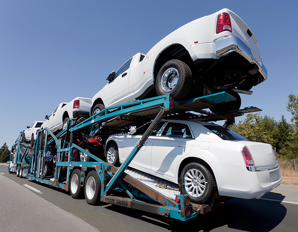 Car transporter carrying four white vehicles on a highway, with a clear blue sky in the background.