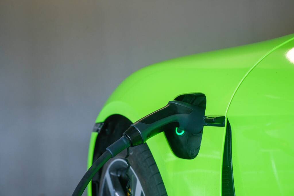 Close-up of a lime green electric car being charged, with the charging cable plugged into the vehicle.