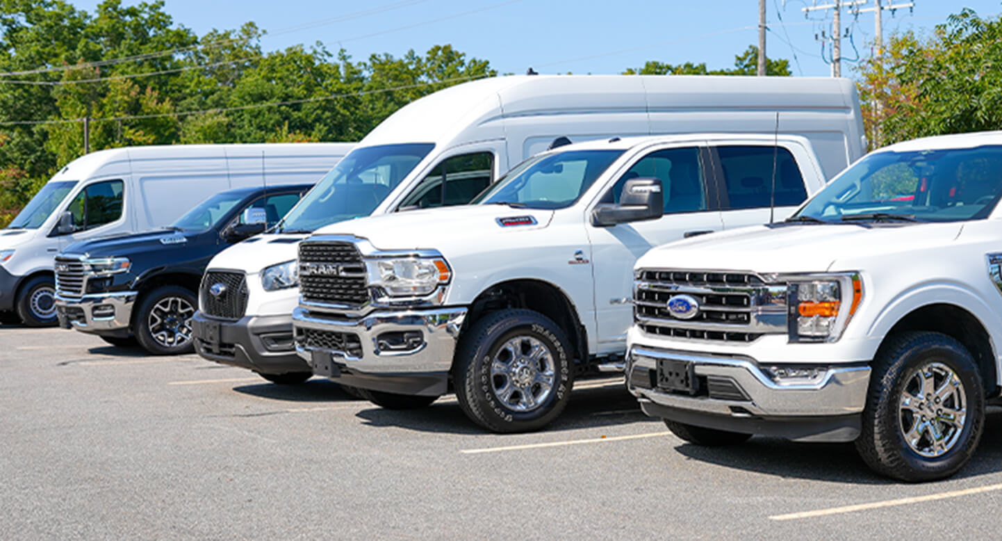 A row of parked white and black trucks and vans in a parking lot on a sunny day.
